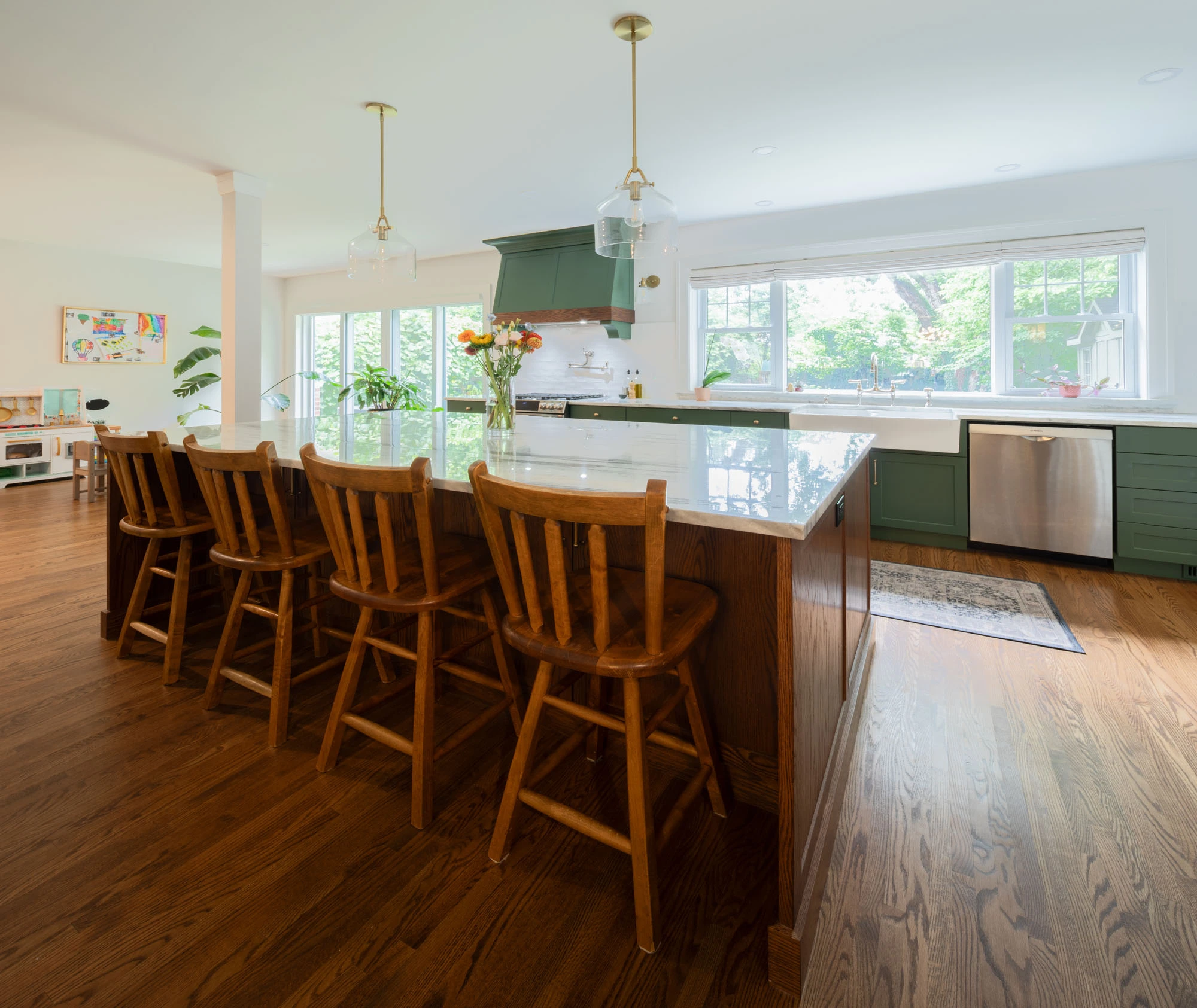 Classic wooden stools lined up against kitchen island with granite countertops. Pendant lighting hangs above the countertop.