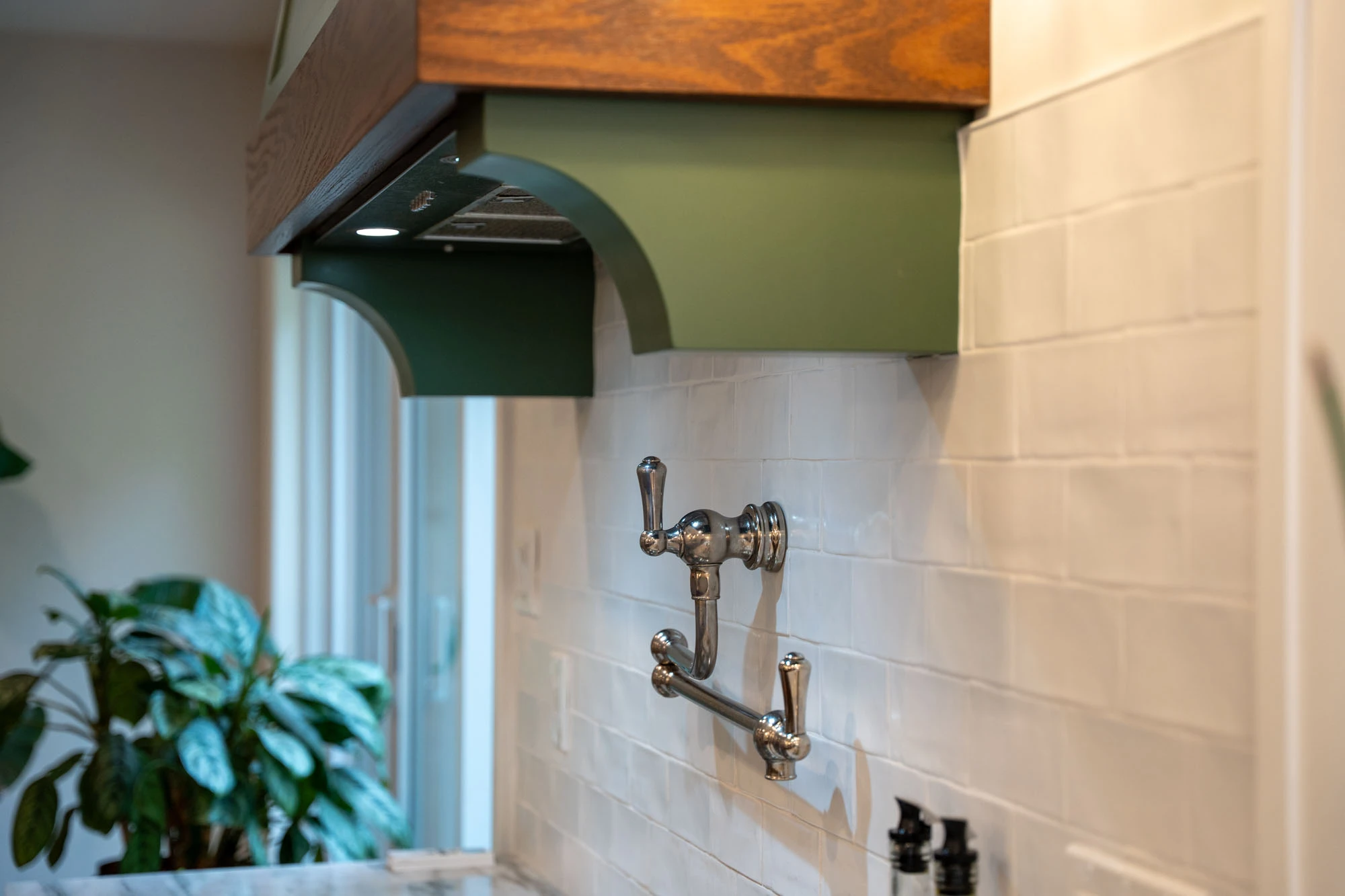 Stovetop range hood and pot filler installed against white tile backsplash.