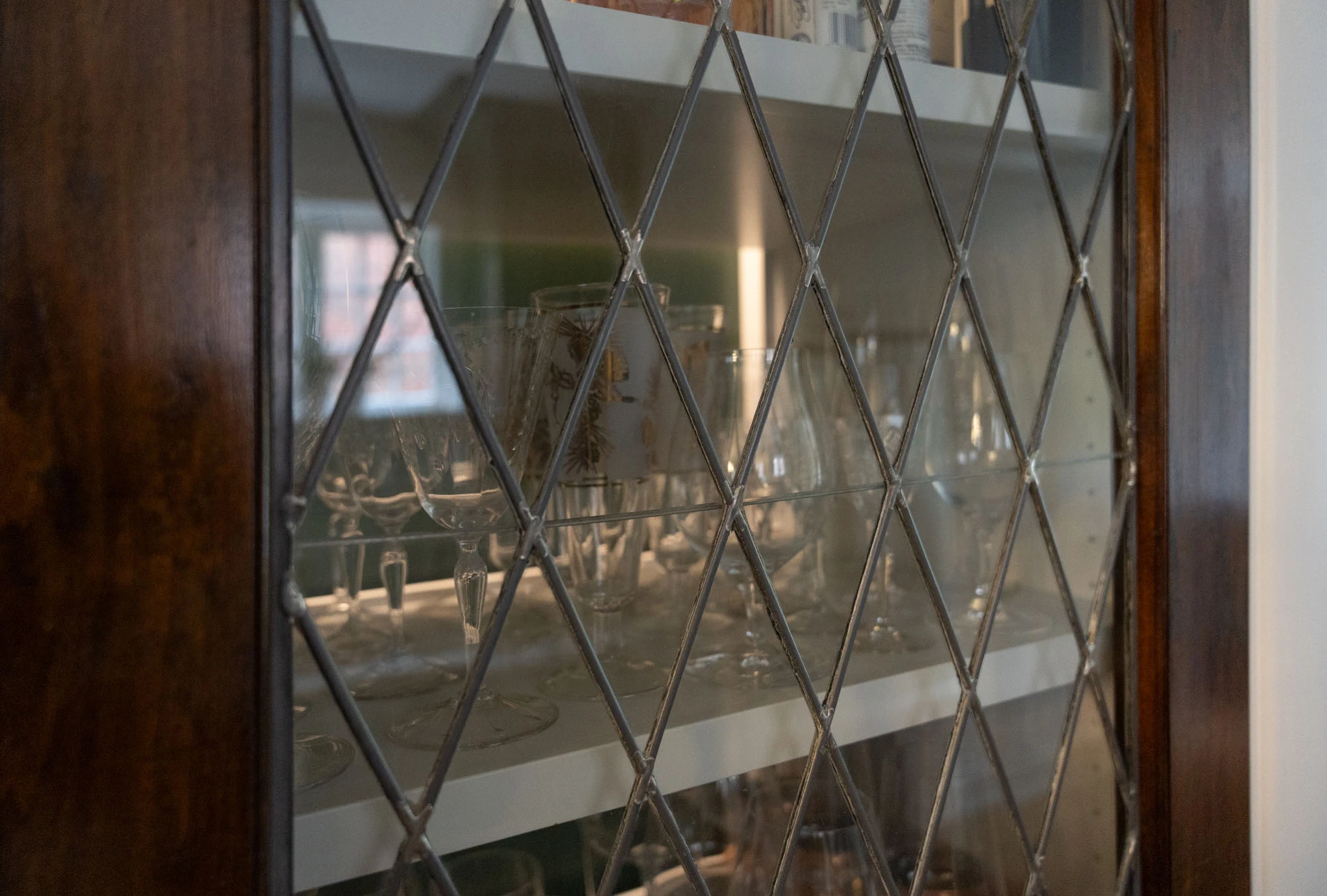Close up of lattice panelled glass door on kitchen cabinet, revealing glassware neatly stacked inside. 