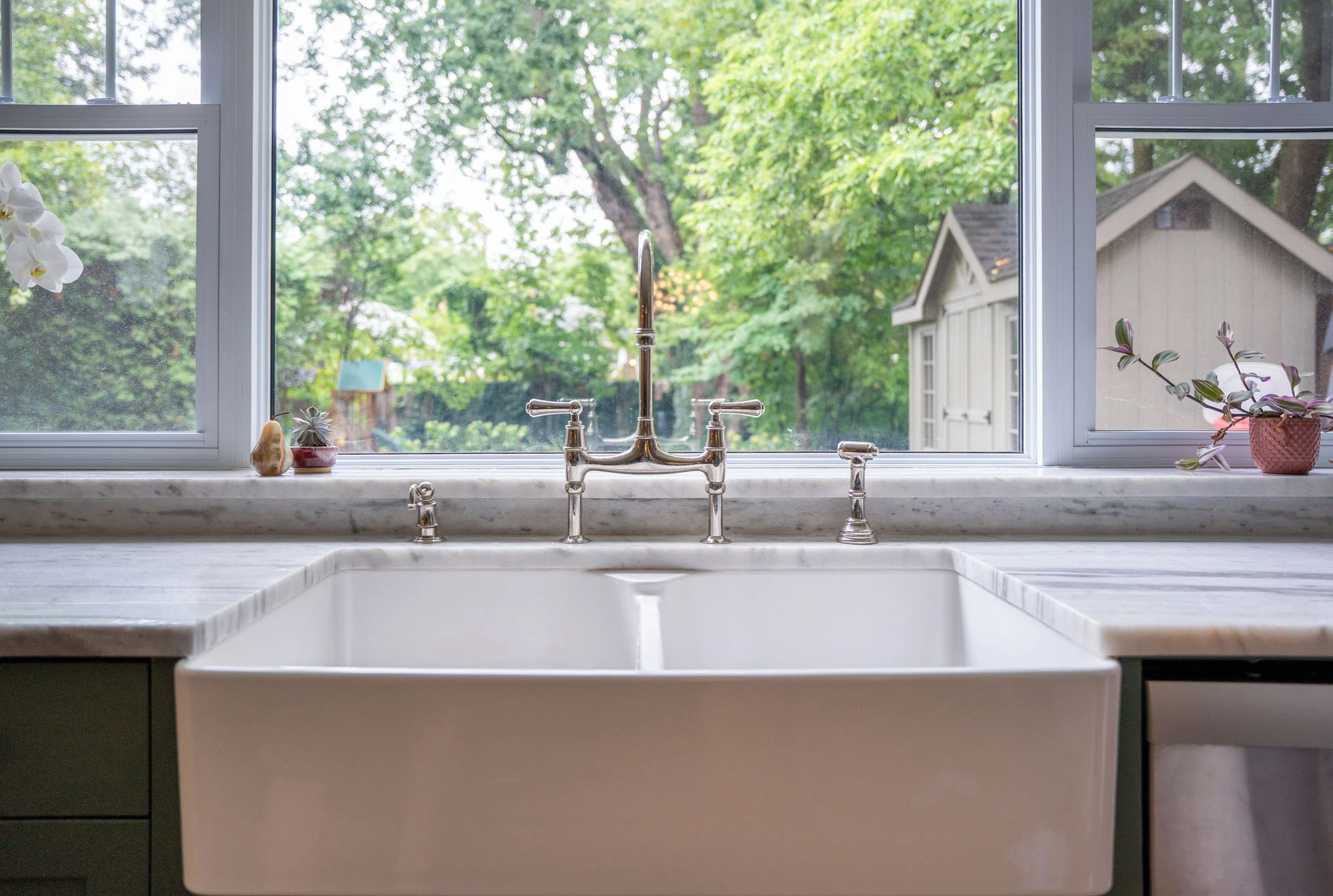 Large picture window leading to backyard, positioned above white kitchen sink.