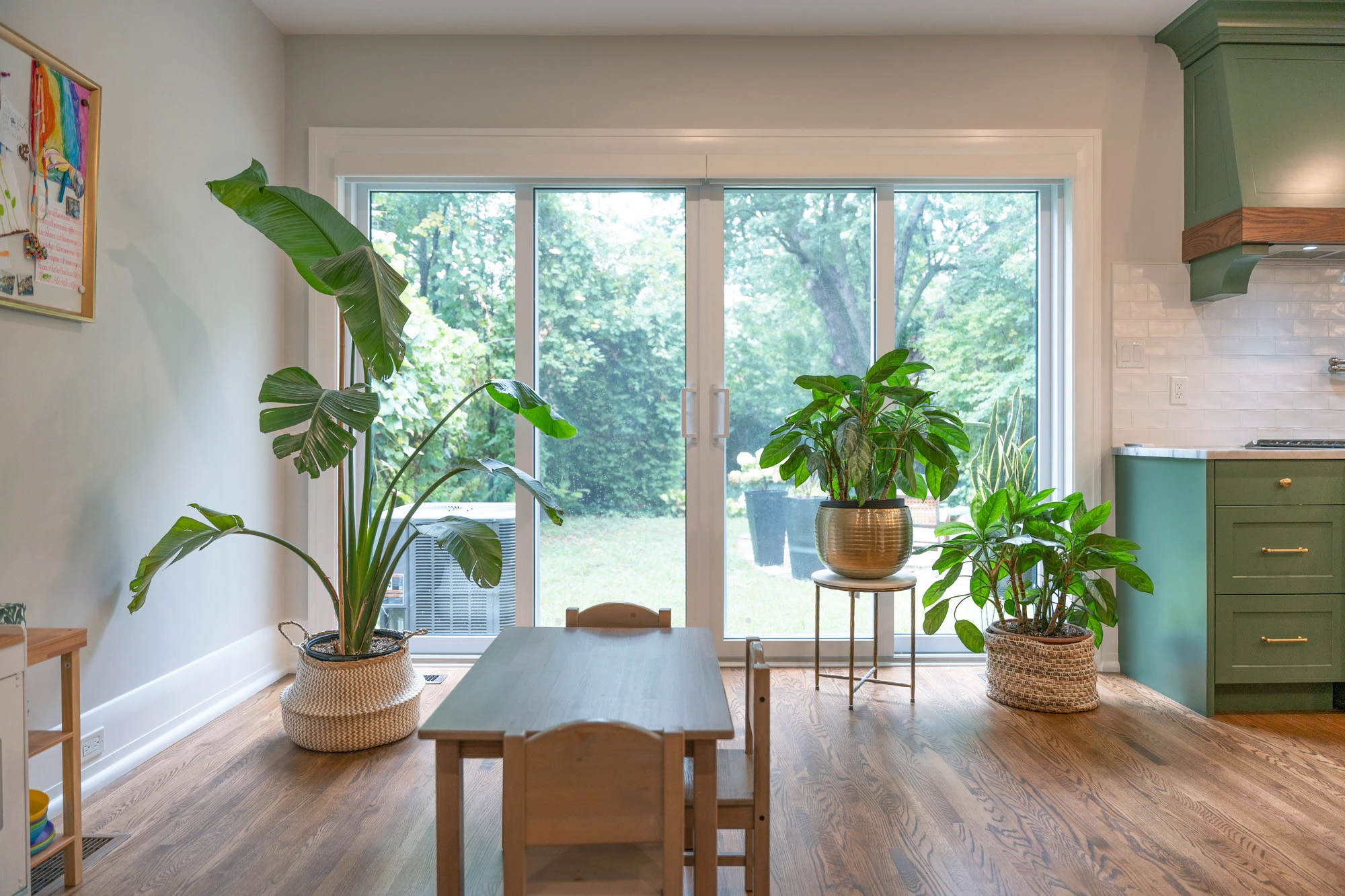 Large glass patio doors alongside kitchen wall, with large plants positioned around it. 