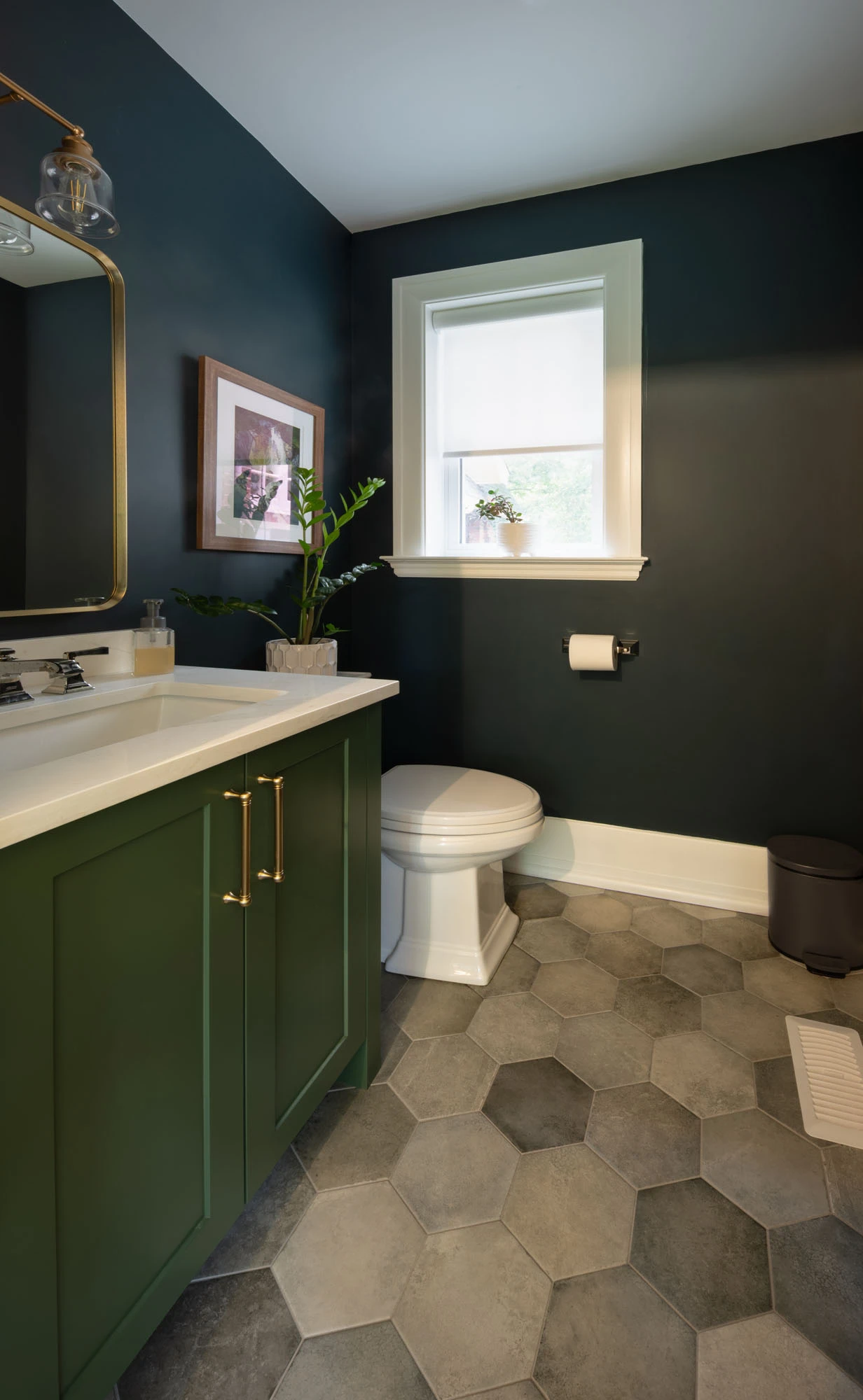 Powder room painted a dramatic navy blue with green cabinetry and hexagonal tiled flooring