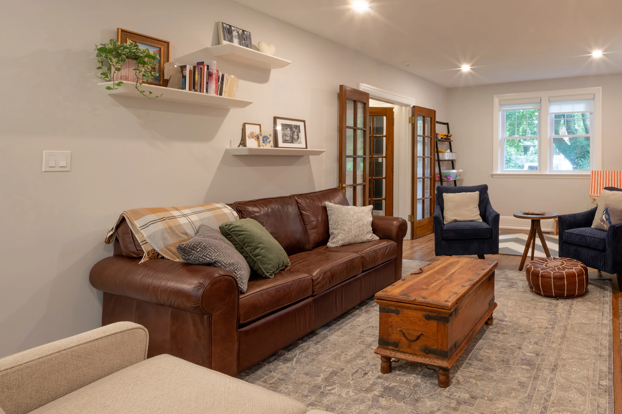 Brown leather couch positioned alongside sitting room wall with floating shelves above