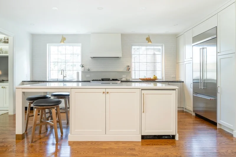 Wide view of kitchen with large island in foreground, white countertops, cabinetry in background.