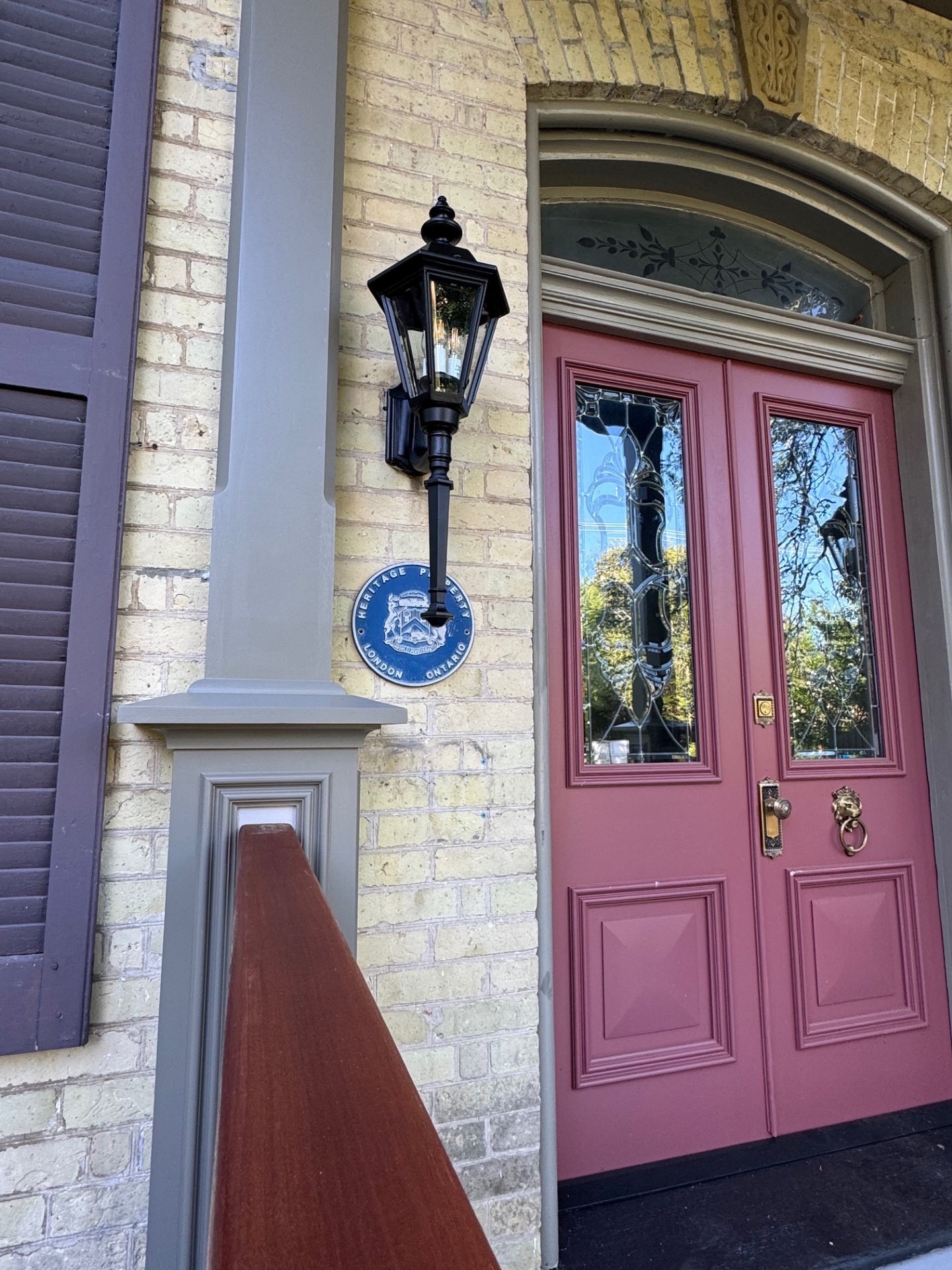 front door in red with classic shutters and railings on a heritage yellow building