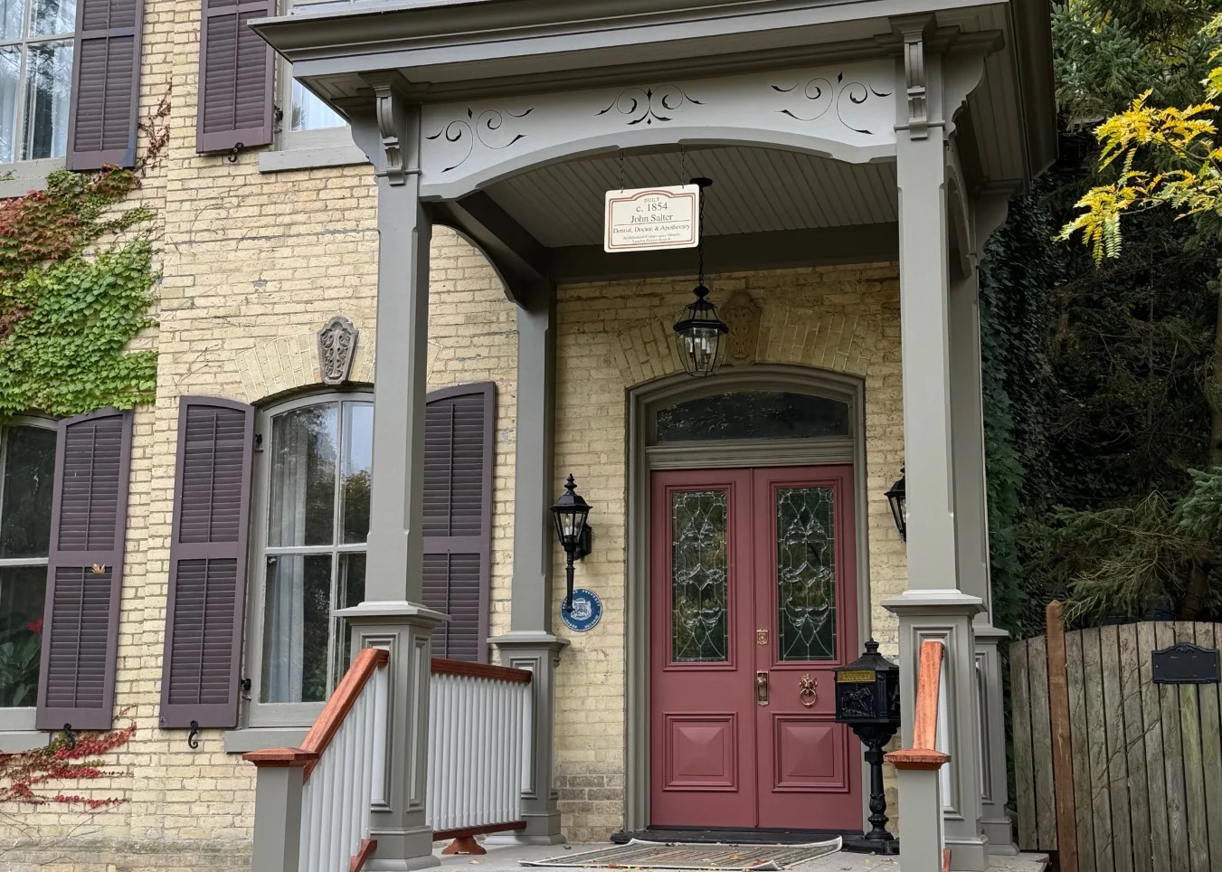 Exterior of heritage home after construction with front deck finished with pale green trim and dark red door