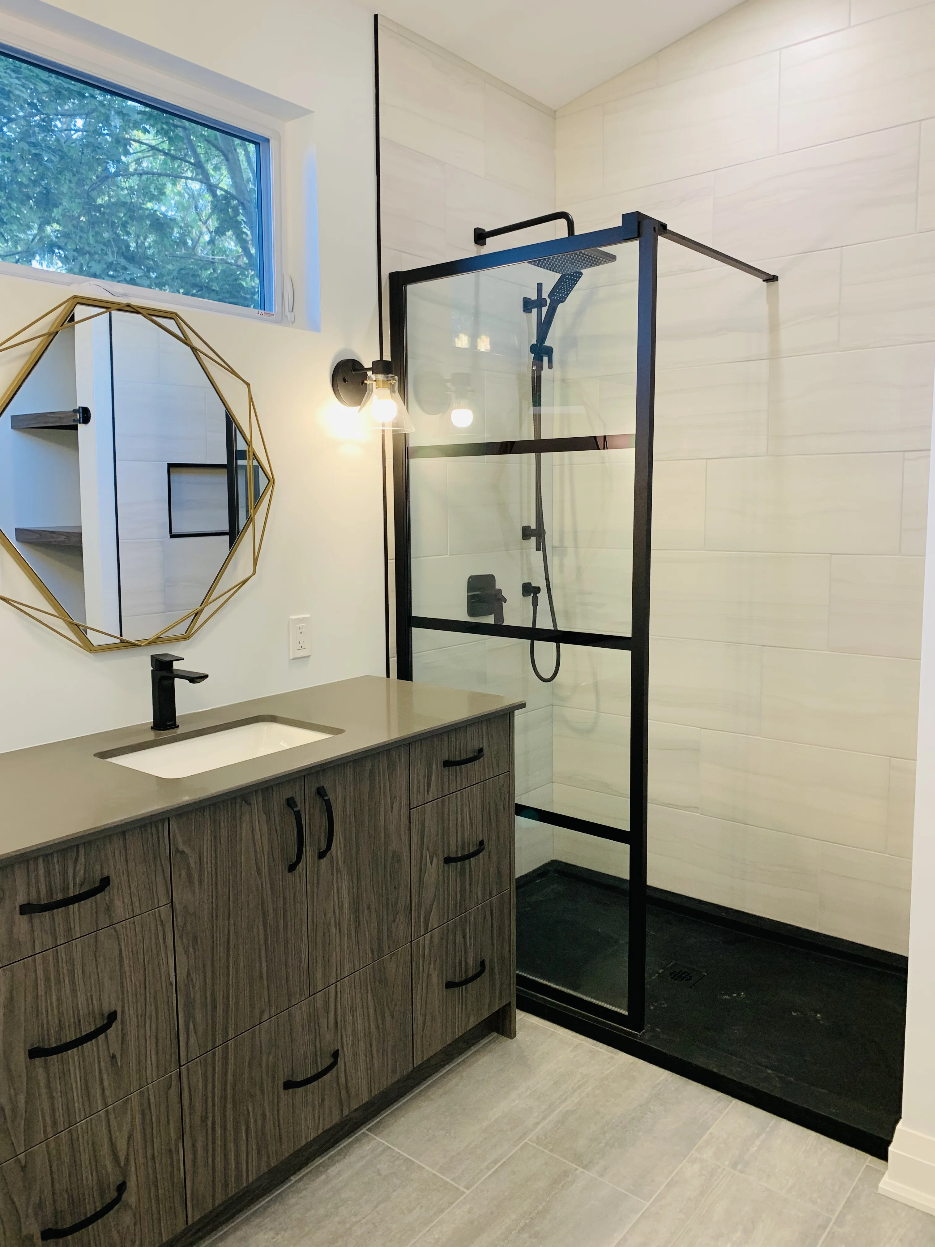 large glass shower with black frame beside the sink with dark countertops and cabinets