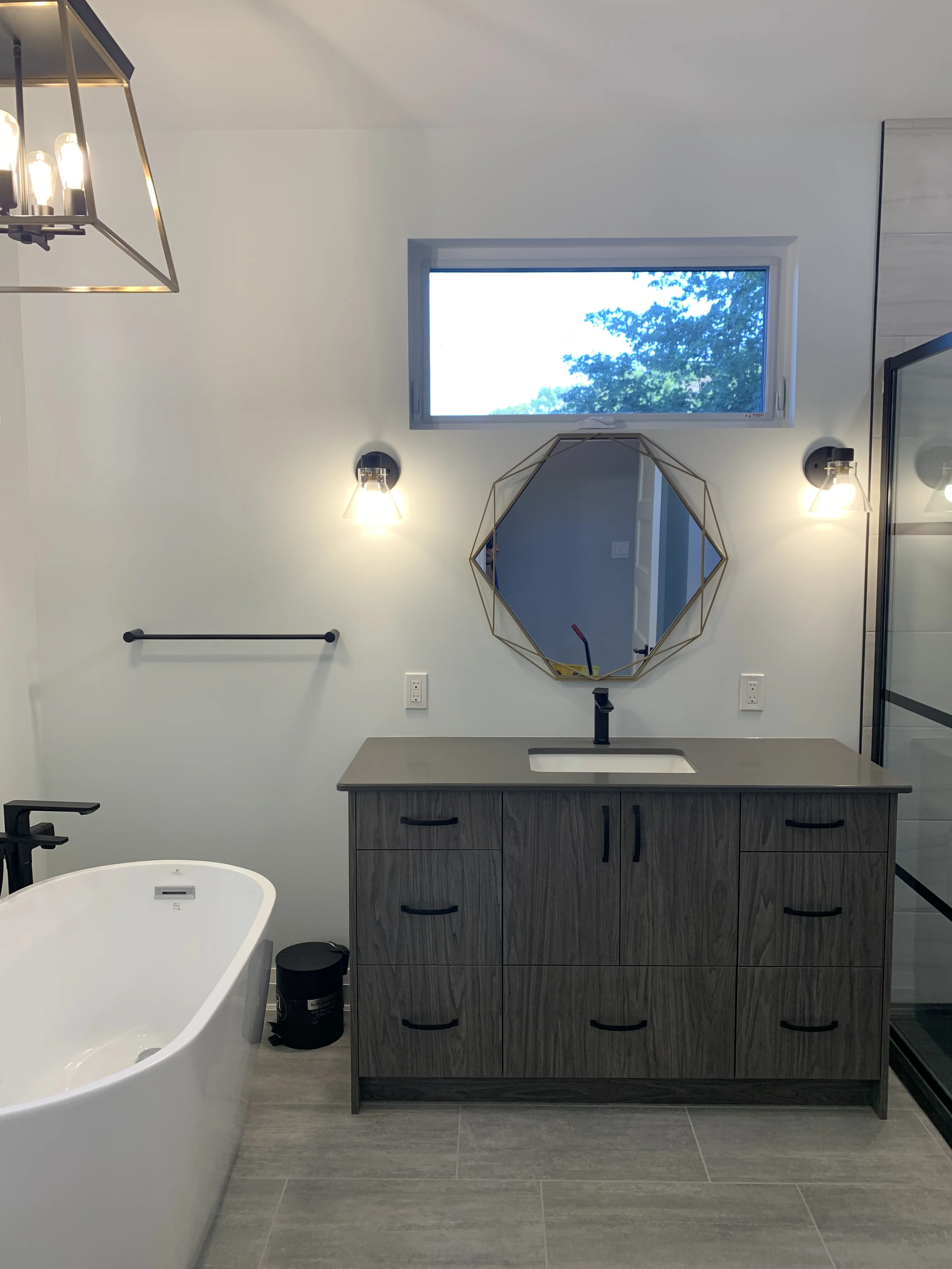 bathroom space with counter and large mirror over a sink, a white tub to one side and a black framed glass shower on the other.