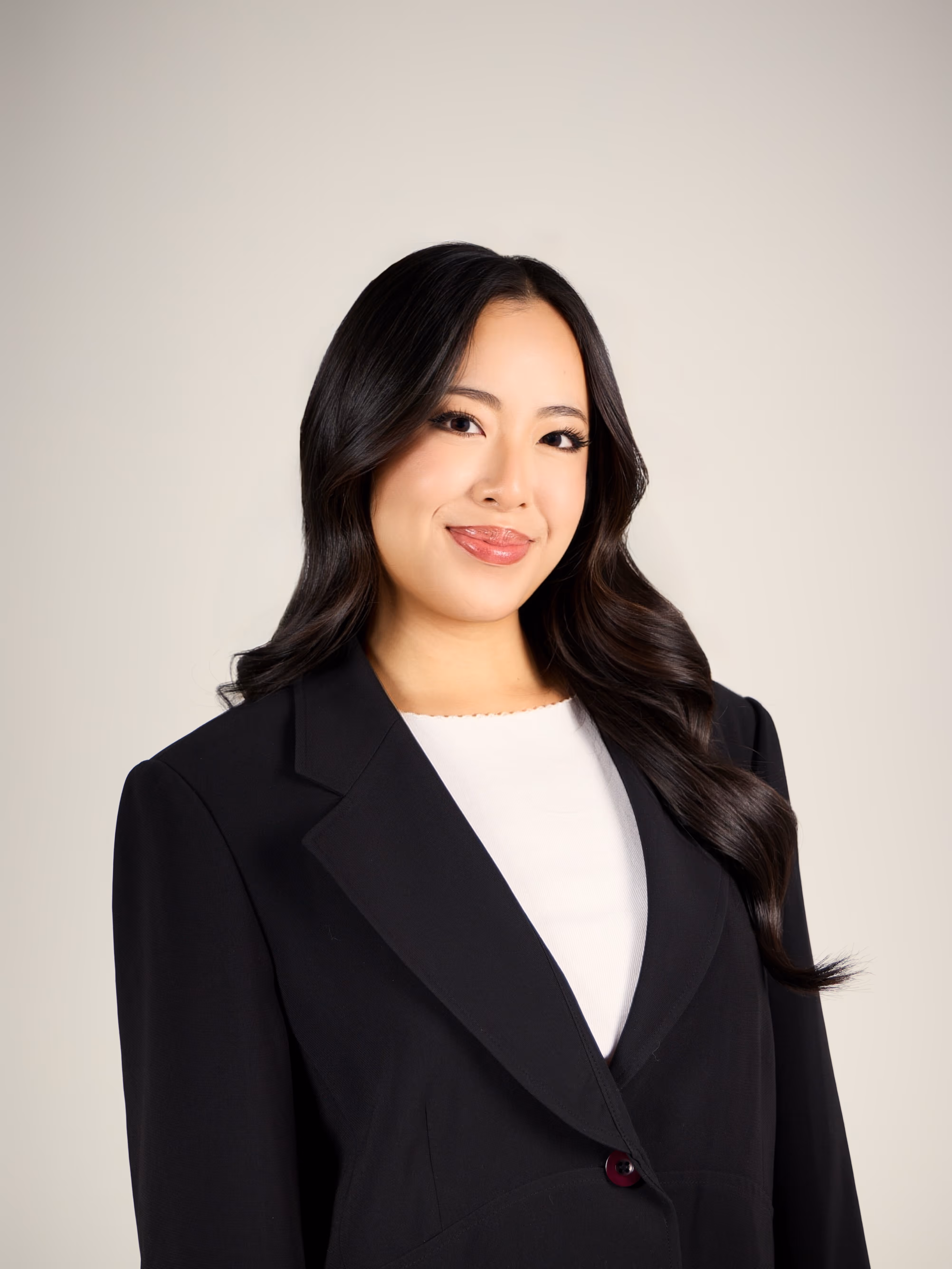 Phoebe smiling with long dark hair wearing a black blazer and white top against a light background.