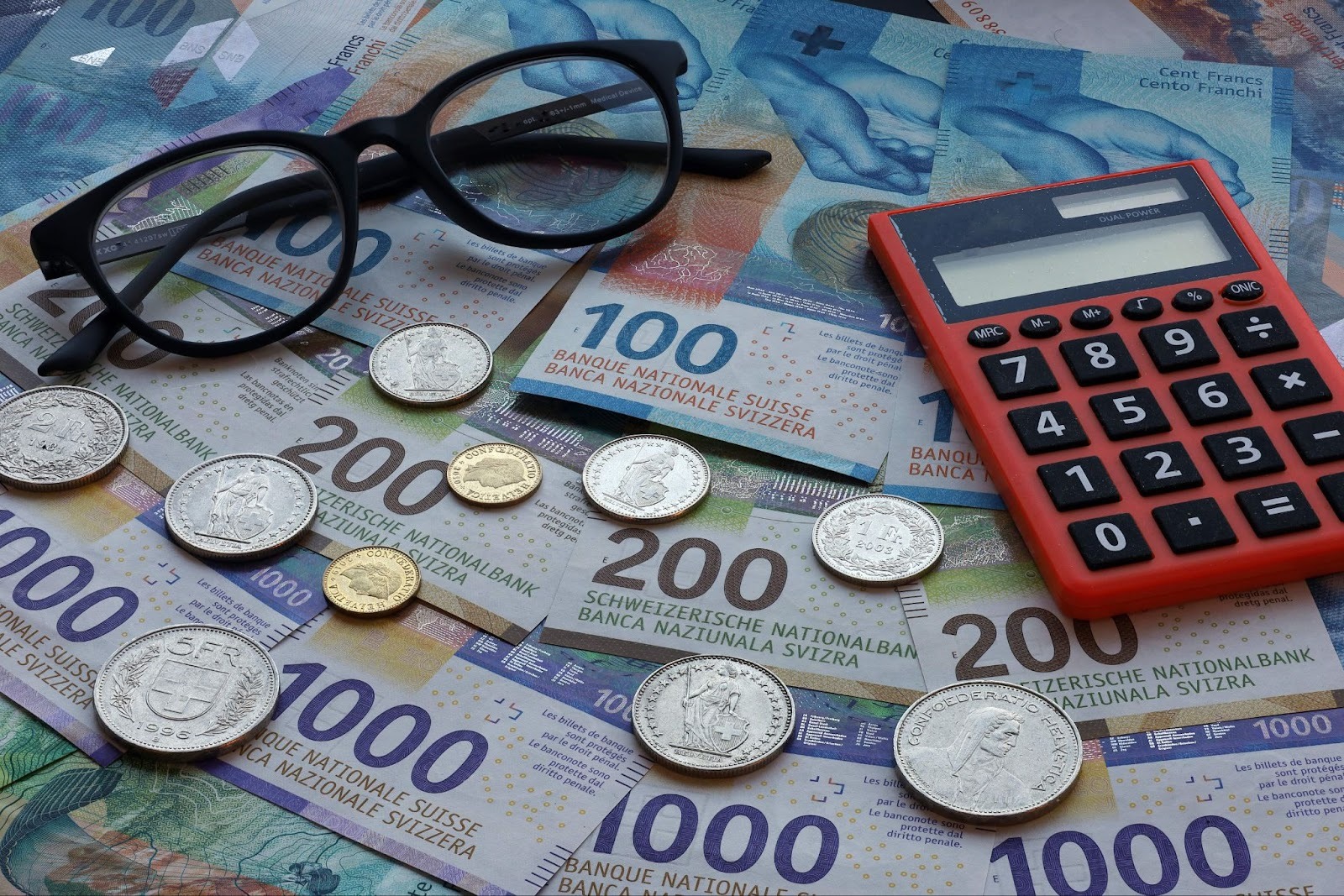 Schweizer Franken Banknoten und Münzen für radicant vs yuh Bankvergleich mit Taschenrechner und Brille