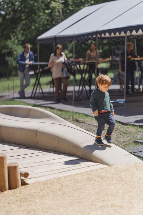 A young child playing on the 3D-printed sandbox bench in Delft, showcasing its smooth, curved design in a vibrant outdoor setting.