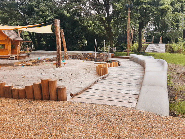 Wide shot of the playground in Delft featuring the 3D-printed sandbox bench and other natural play elements in a sunny outdoor space