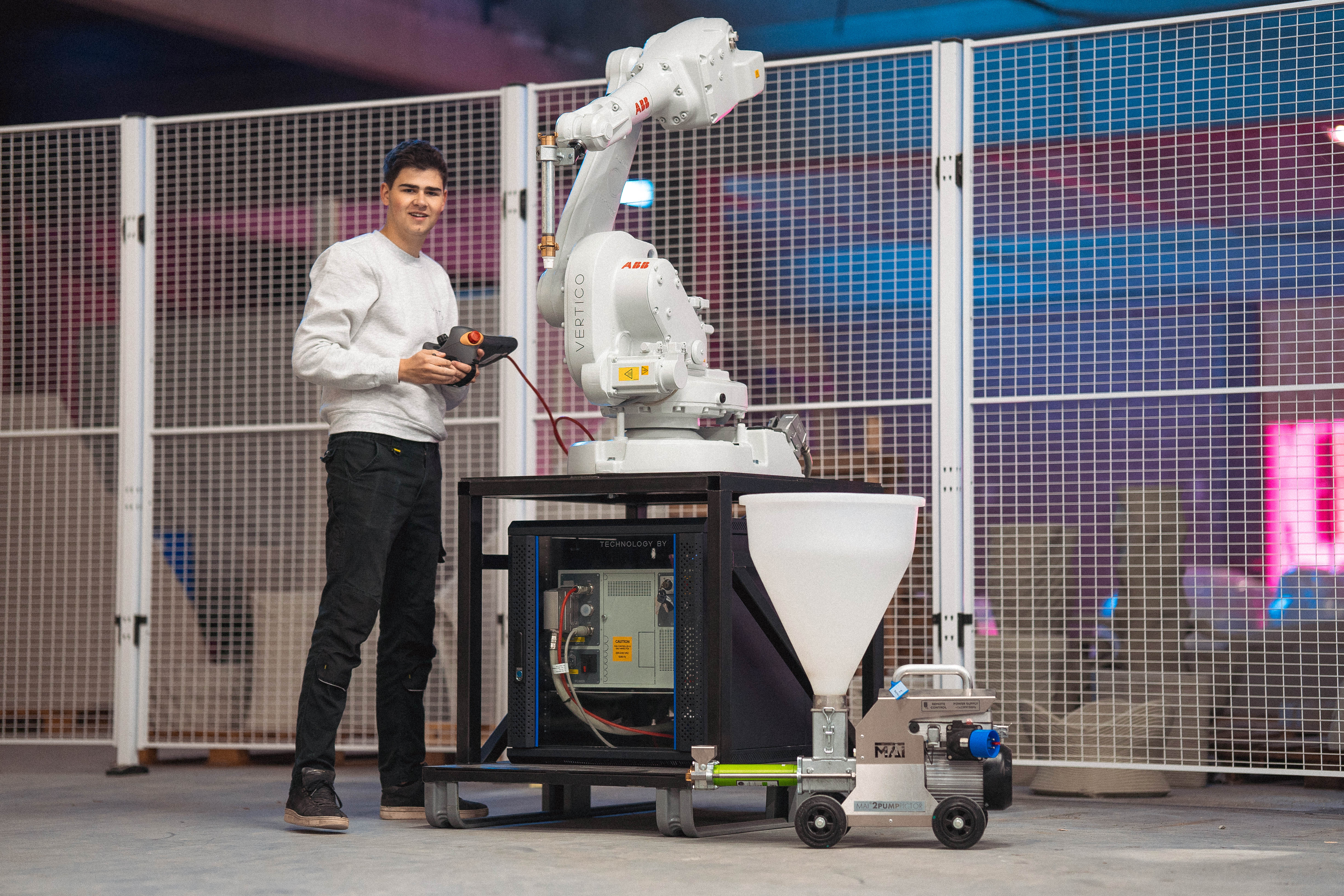 Technician operates white ABB robotic arm with remote control in industrial setting