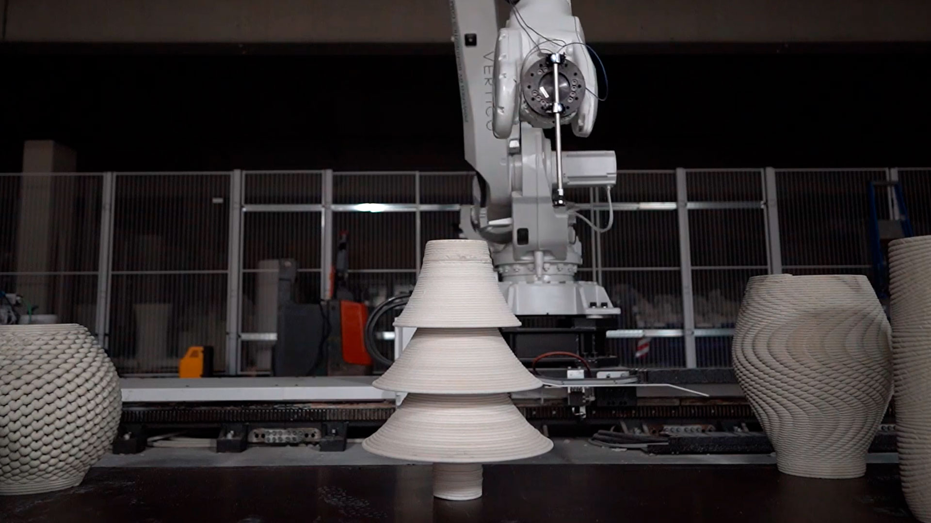 3D concrete printing robot creating layered bell-shaped object in workshop