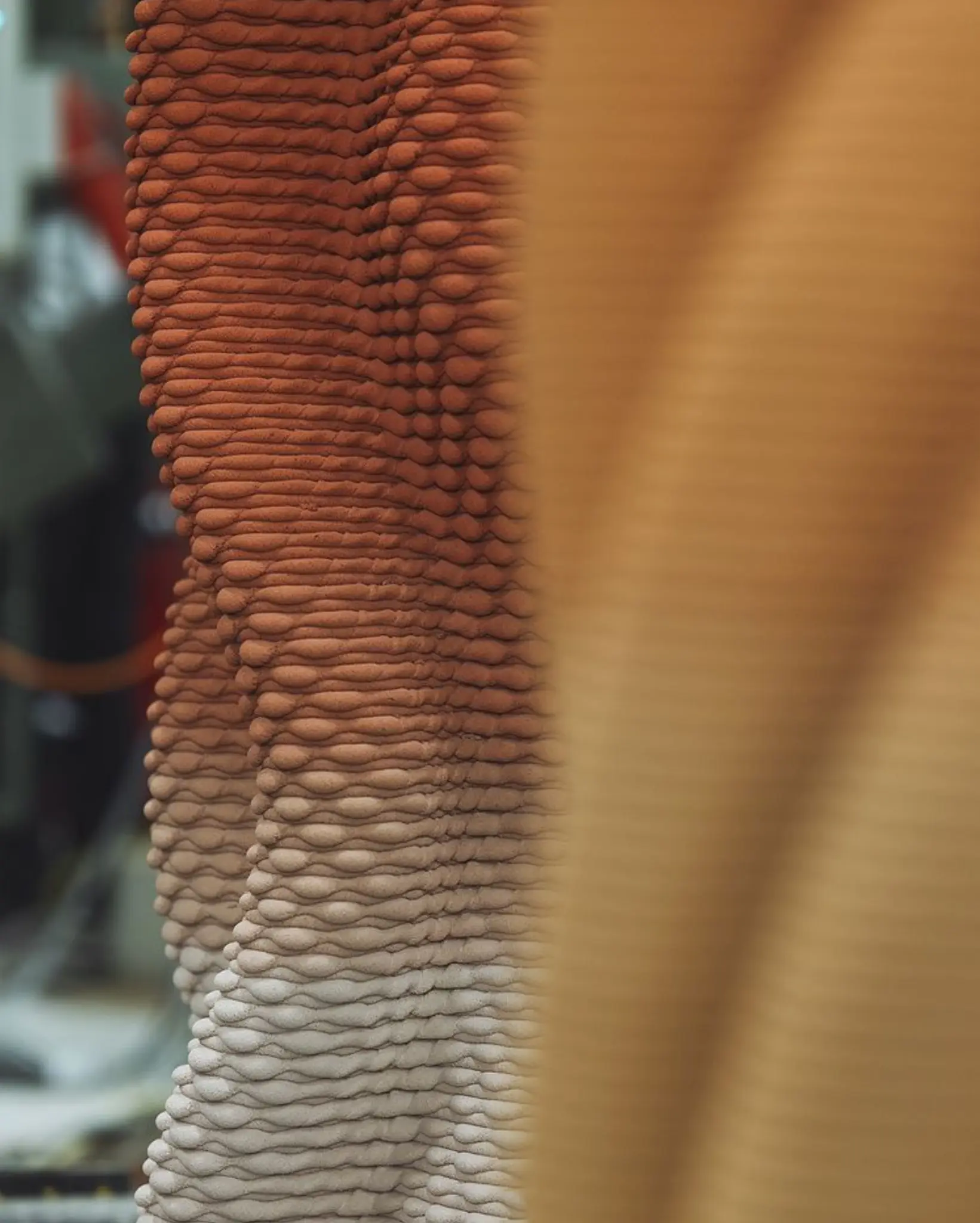 3D concrete printing creating textured, layered wall with gradient color