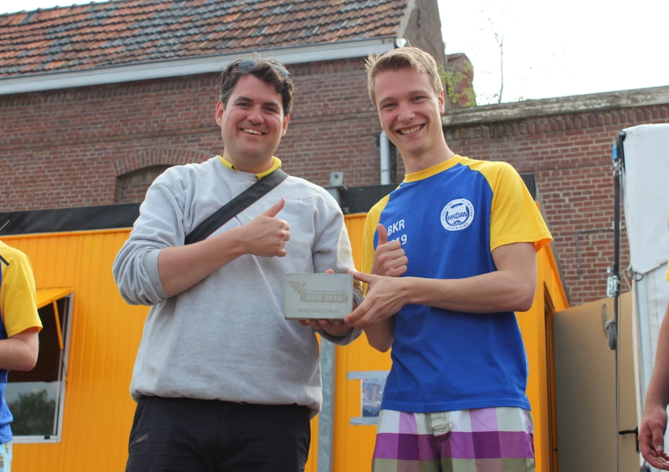 Students with concrete printing projects, giving thumbs up near brick building