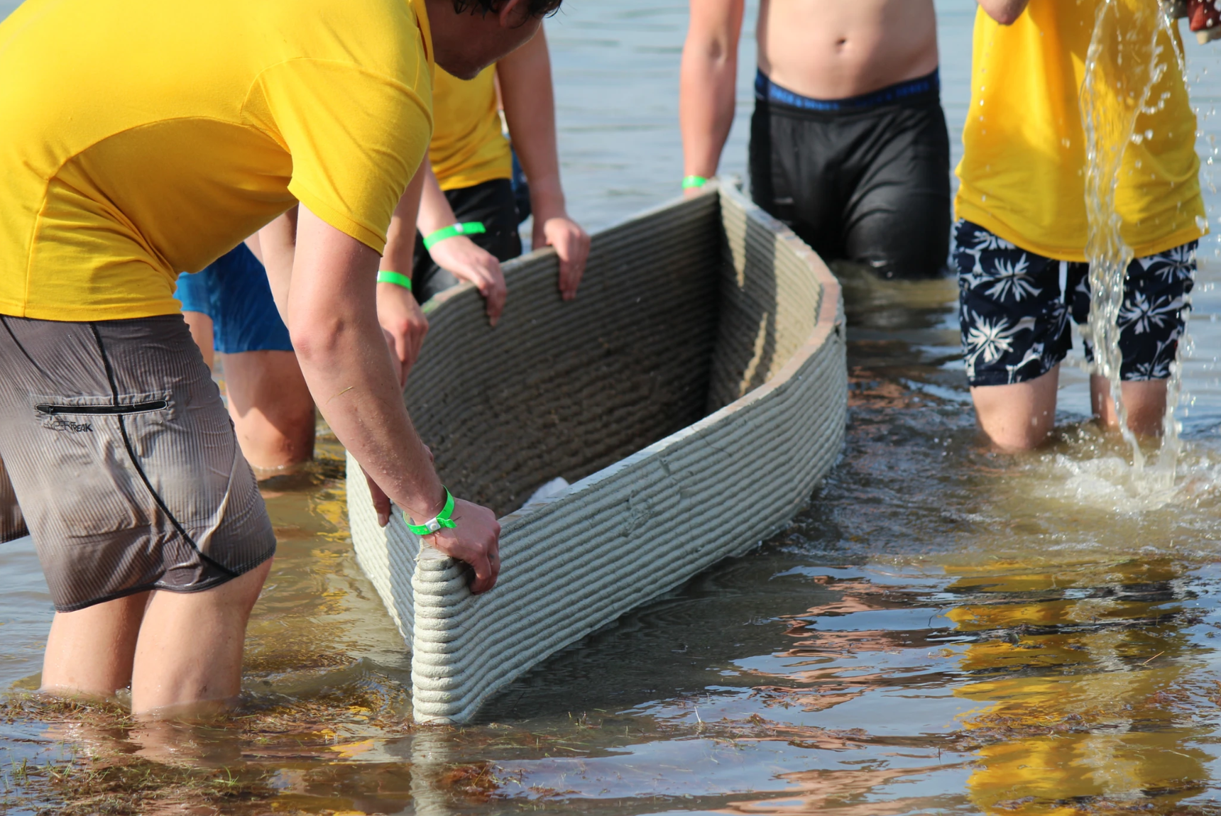 Concrete boat printing project with team in yellow shirts wading in water