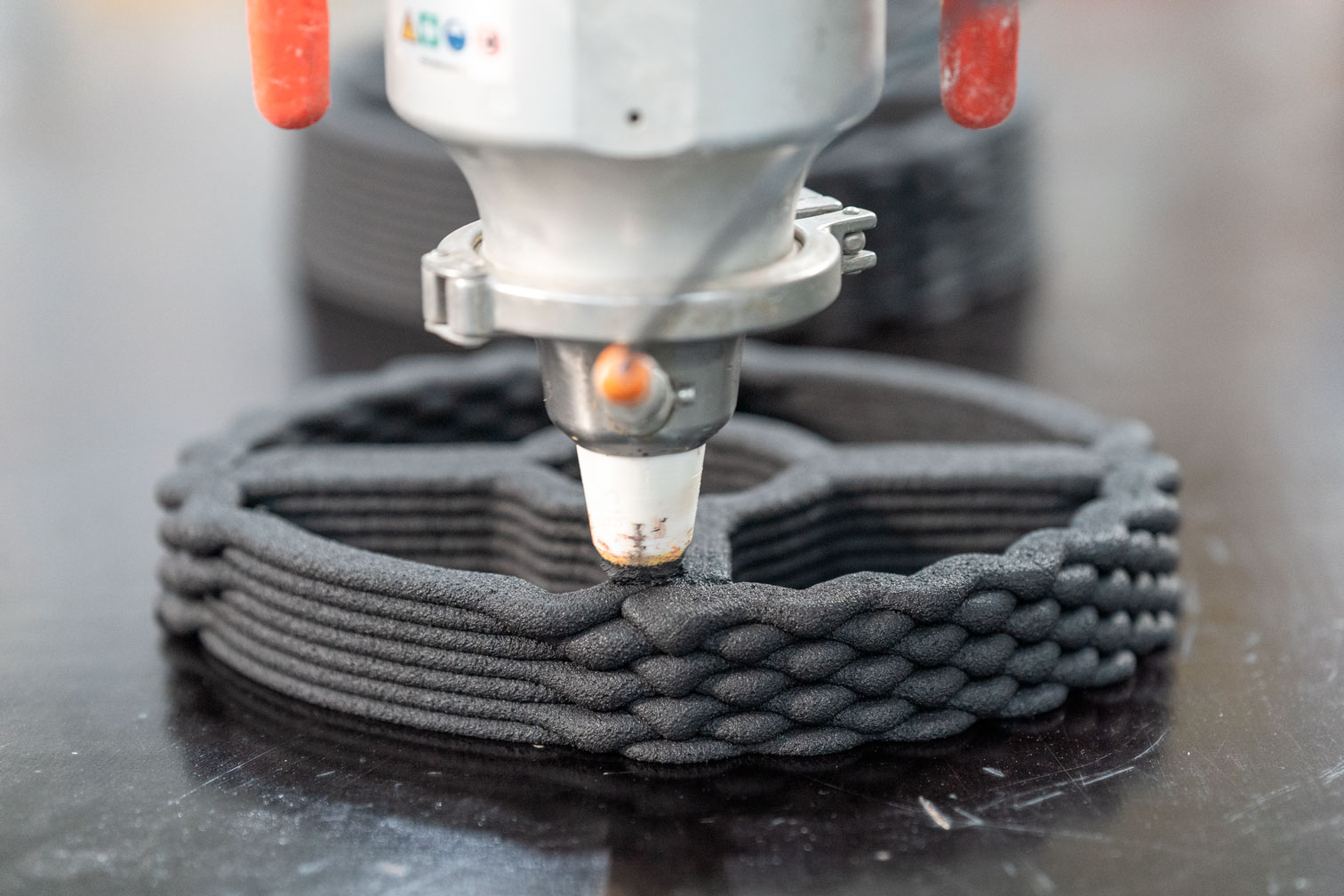 3D printer creating a layered dark object with orange print nozzle