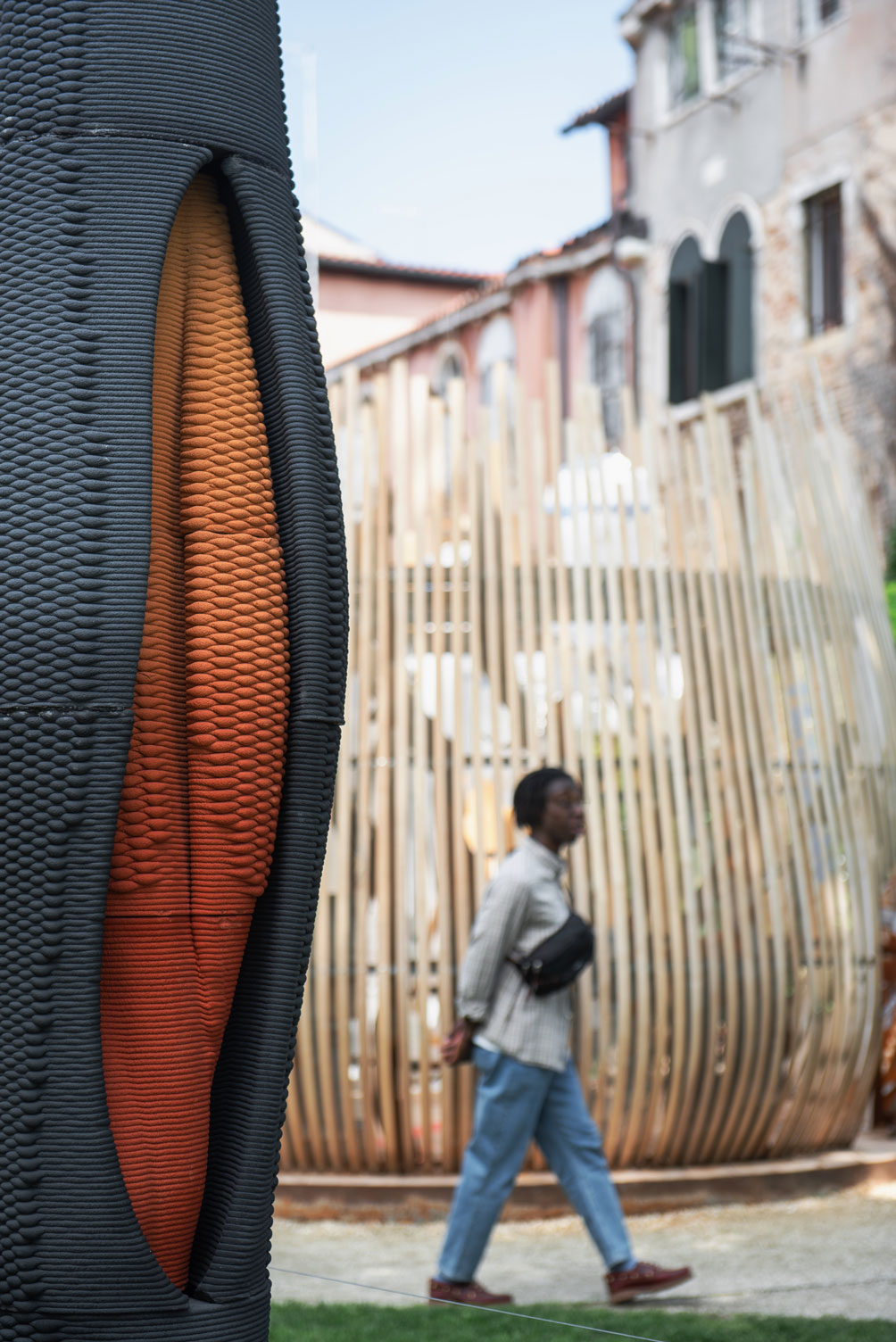 Black and orange textured column with person walking by wooden fence