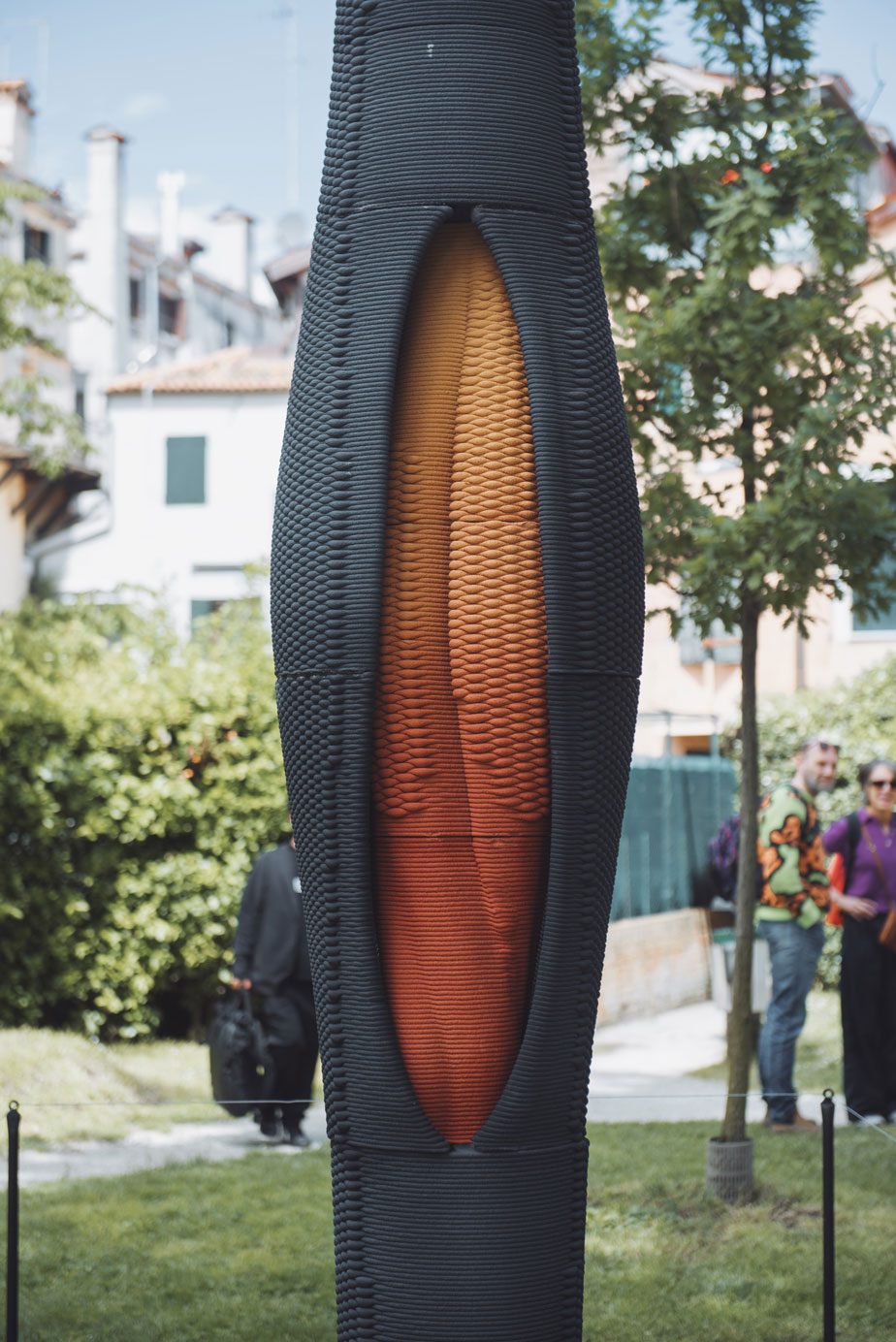 Modern sculptural column with orange-red core in urban garden setting