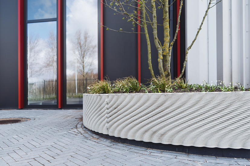 Modern white curved planter with tree and plants near glass building