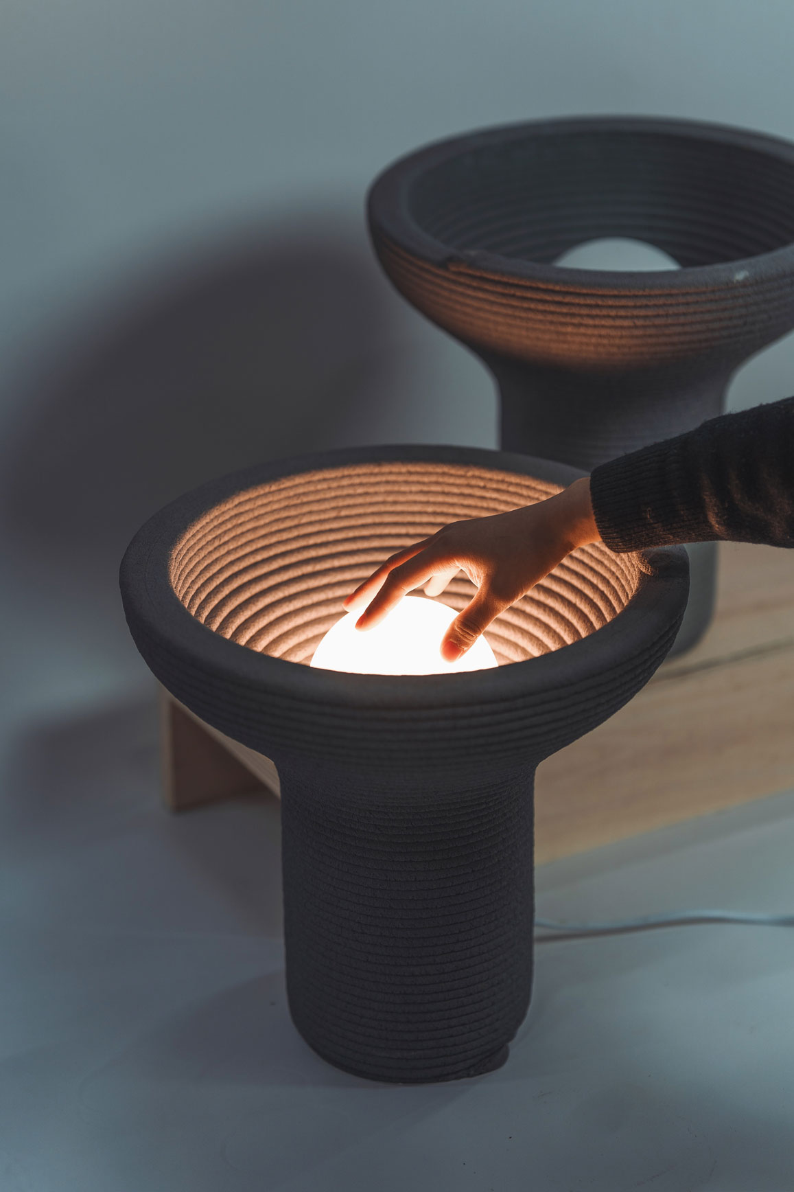 Hand touching glowing ceramic lamp with ribbed design and warm light