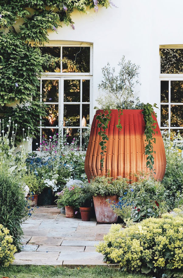 Large 3D printed concrete planter among lush garden with stone pathway