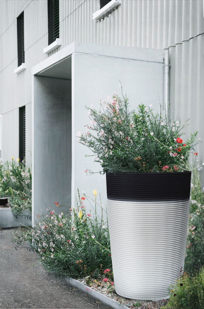 3D printed concrete planter with colorful flowers near modern building