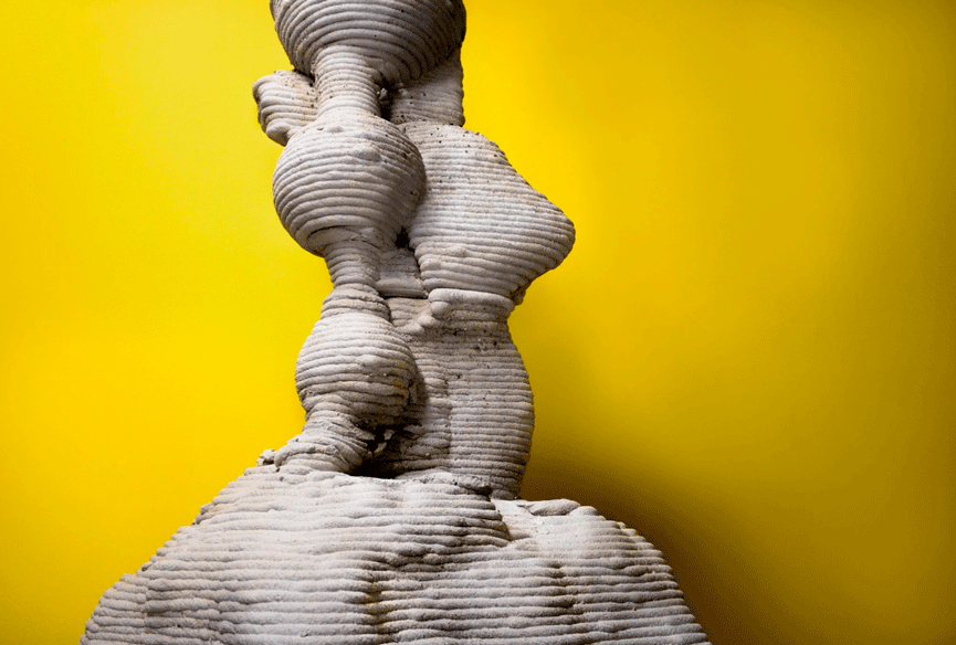 Textured stone sculpture of twisted human form against bright yellow background