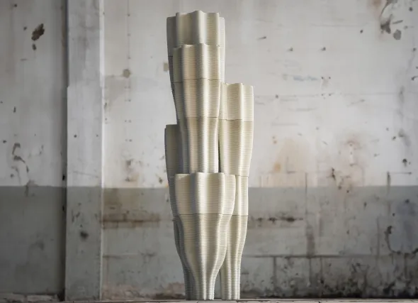 Tall metallic sculpture with curved, stacked cylindrical forms against concrete
