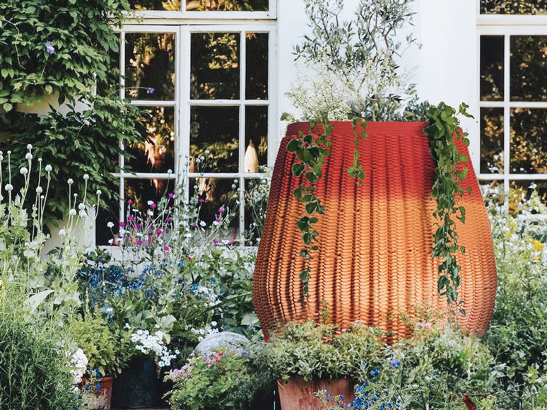 Large red woven basket surrounded by lush garden and white windowed building