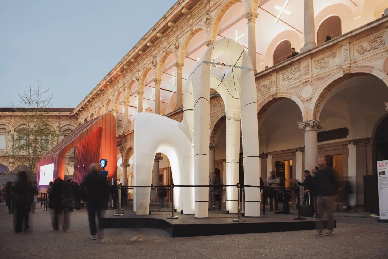 White sculptural installation in historic arched courtyard with blurred visitors