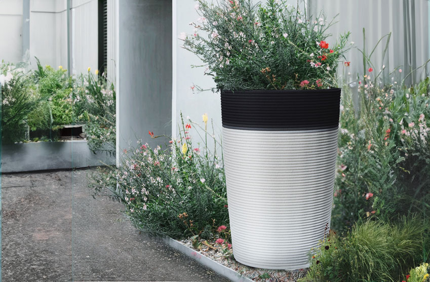 Large white and black planter with red and pink flowers near modern building