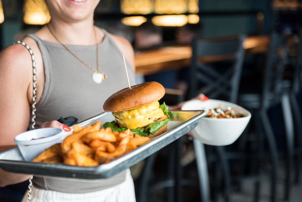 A server carrying a tray with a cheeseburger and fries at The Caz