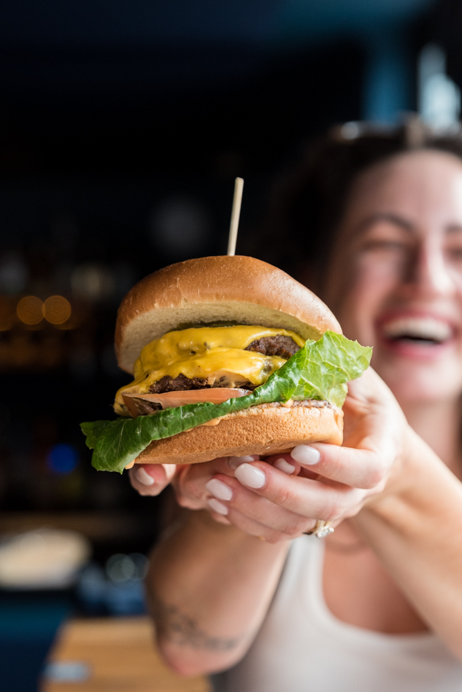 A smiling guest holding up a cheeseburger at The Caz