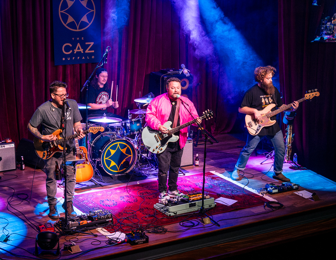 A four-piece rock band performing on stage at The Caz