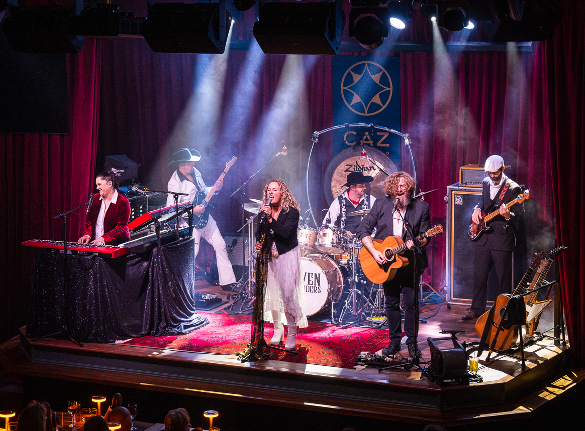 A band with keyboards and acoustic guitar performing on stage at The Caz