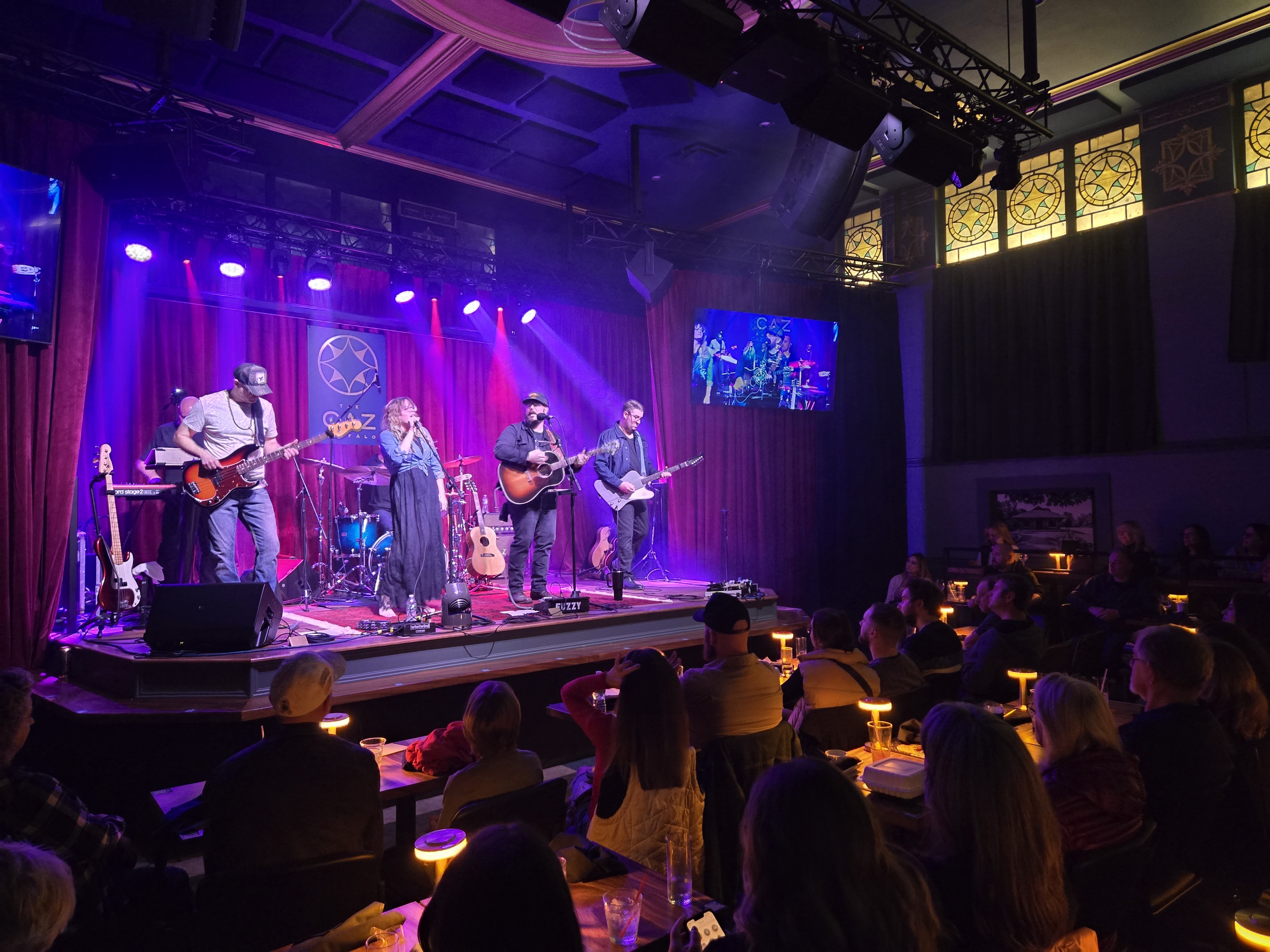 A band performing on stage to a seated audience at The Caz