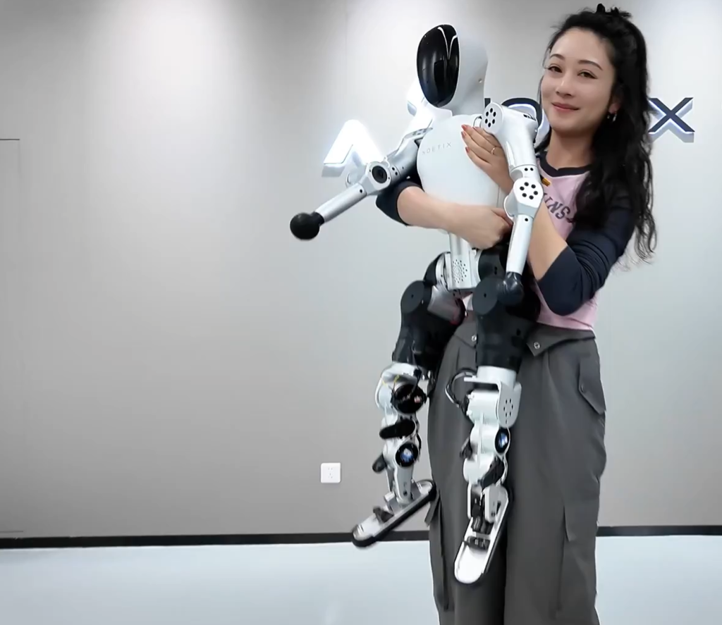 Noetix Robotics employee demonstrating Bumi humanoid robot's portable 12kg weight by holding complete robot in arms at company facility, robot's 94cm height shown relative to adult woman's torso reaching from hip to shoulder level, white and silver robot body with black head visor, articulated limbs hanging naturally showing joint flexibility, demonstrating lightweight composite construction enabling single-person transport without equipment, Noetix logo partially visible in background