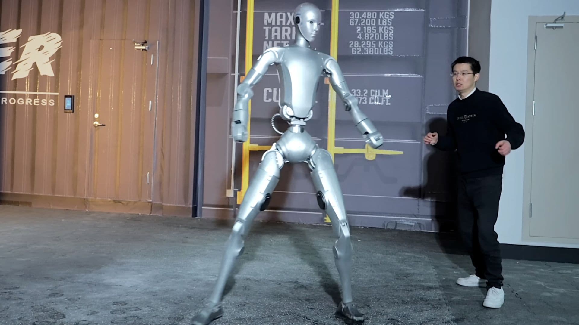 Unitree H2 Destiny Awakening humanoid robot in training facility next to engineer, showing full 182cm human-scale height - $29,900, available April 2026 in USA and Canada