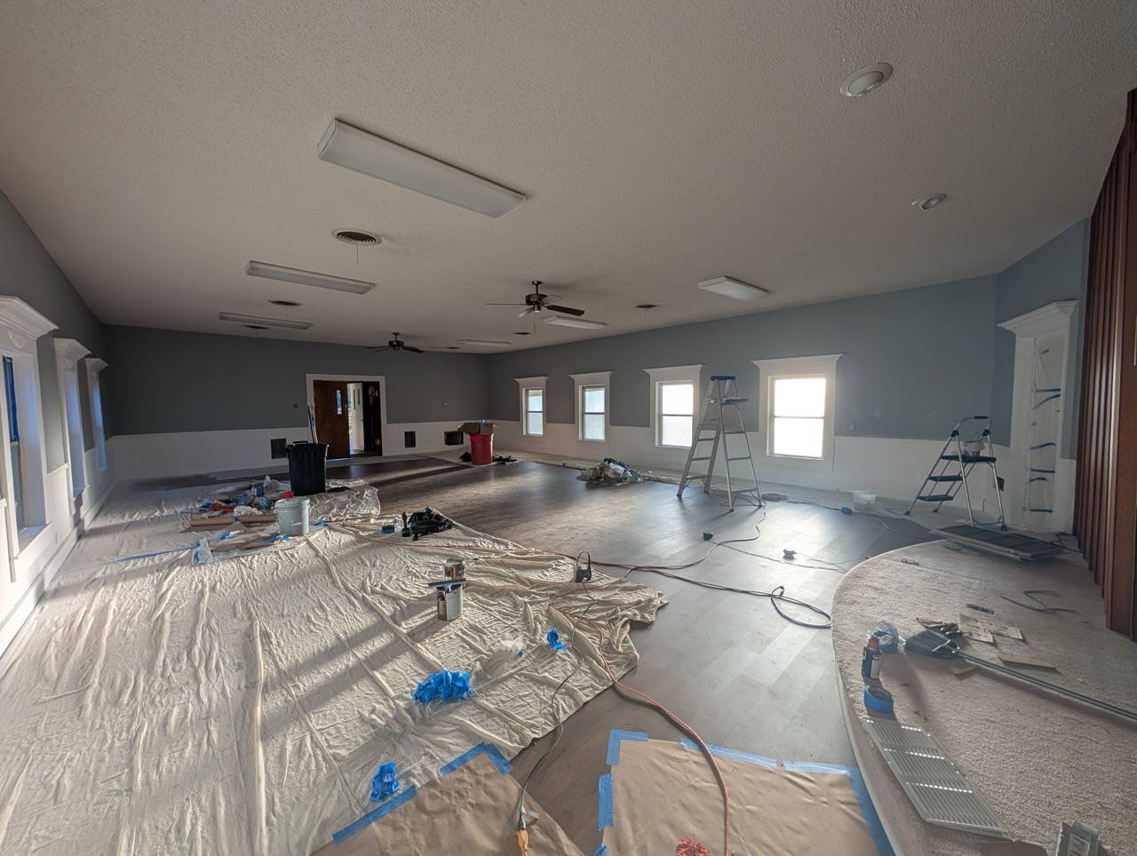 Living room and kitchen area with gray couches, packed U-Haul moving boxes, and a blue and red child’s chair near a large window.