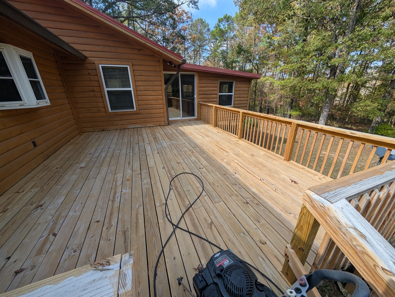 New wooden deck attached to a log cabin with railing and an electric lawn mower on it.