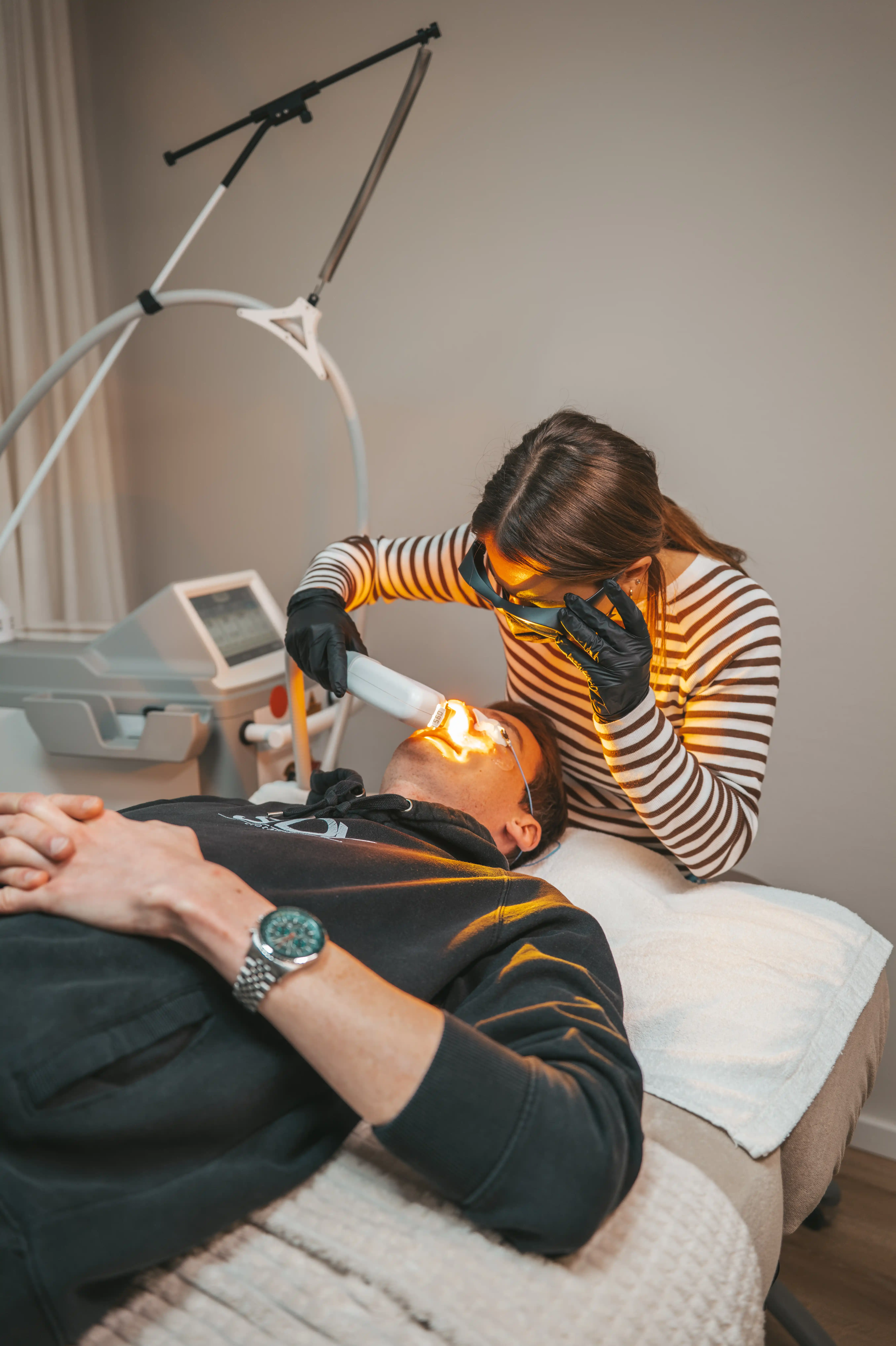 Kosmetikerin führt eine Laserbehandlung im Gesicht eines liegenden Mannes durch.