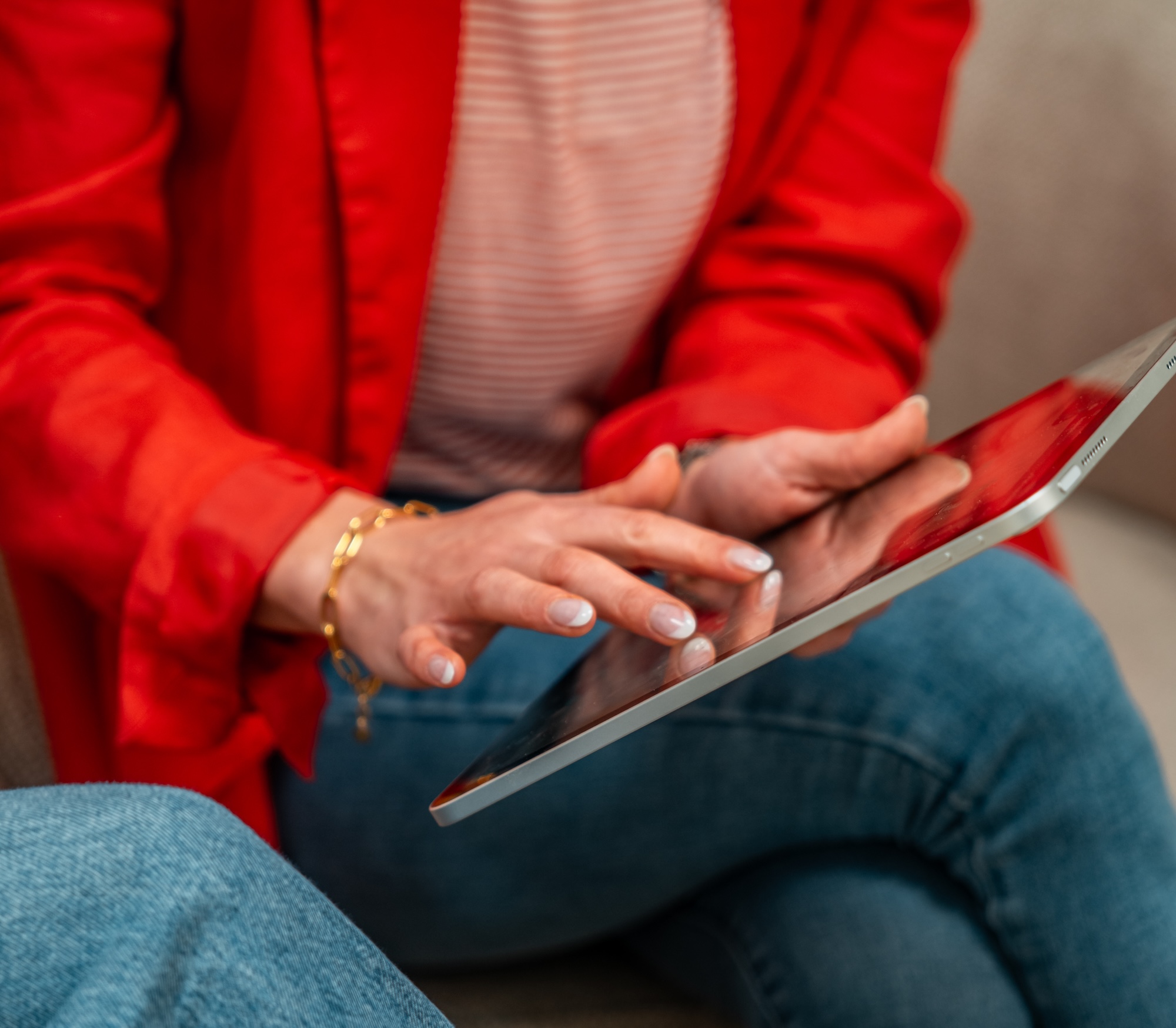 Person in rotem Blazer und Jeans bedient ein Tablet mit den Fingern.