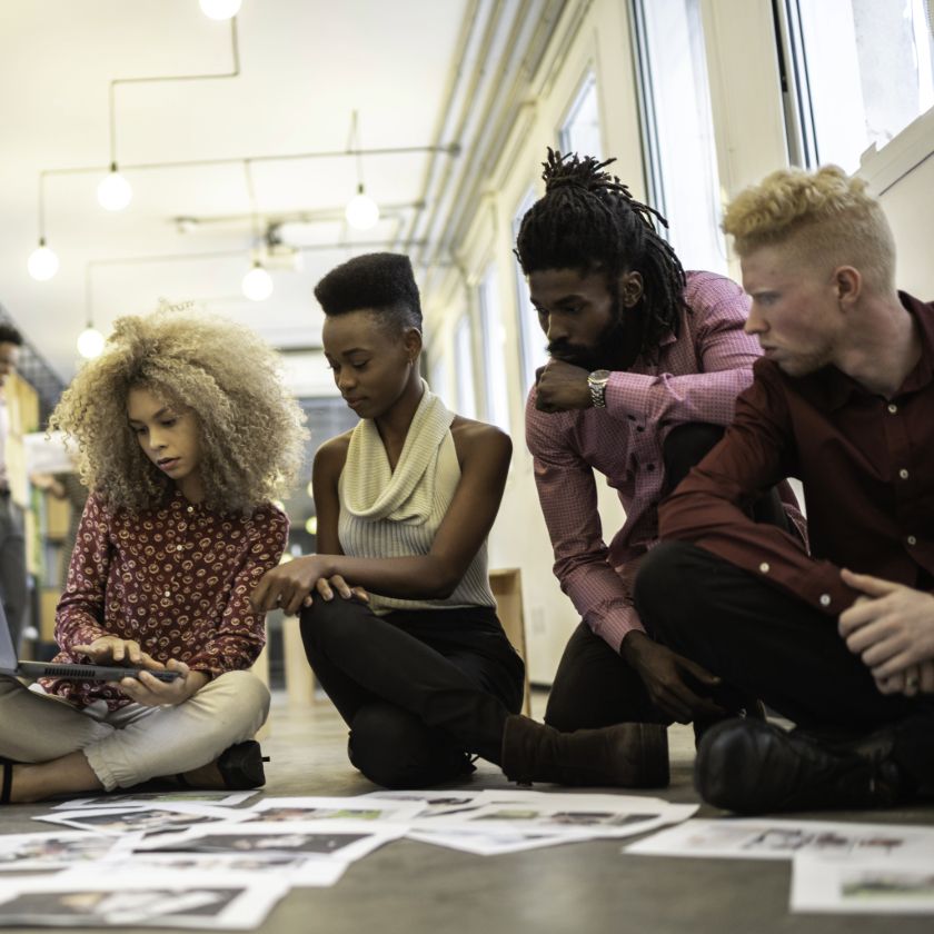 A group of people gather looking at scattered files while sitting on the floor.
