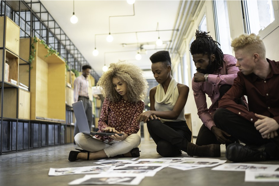A group of people gather looking at scattered files while sitting on the floor.