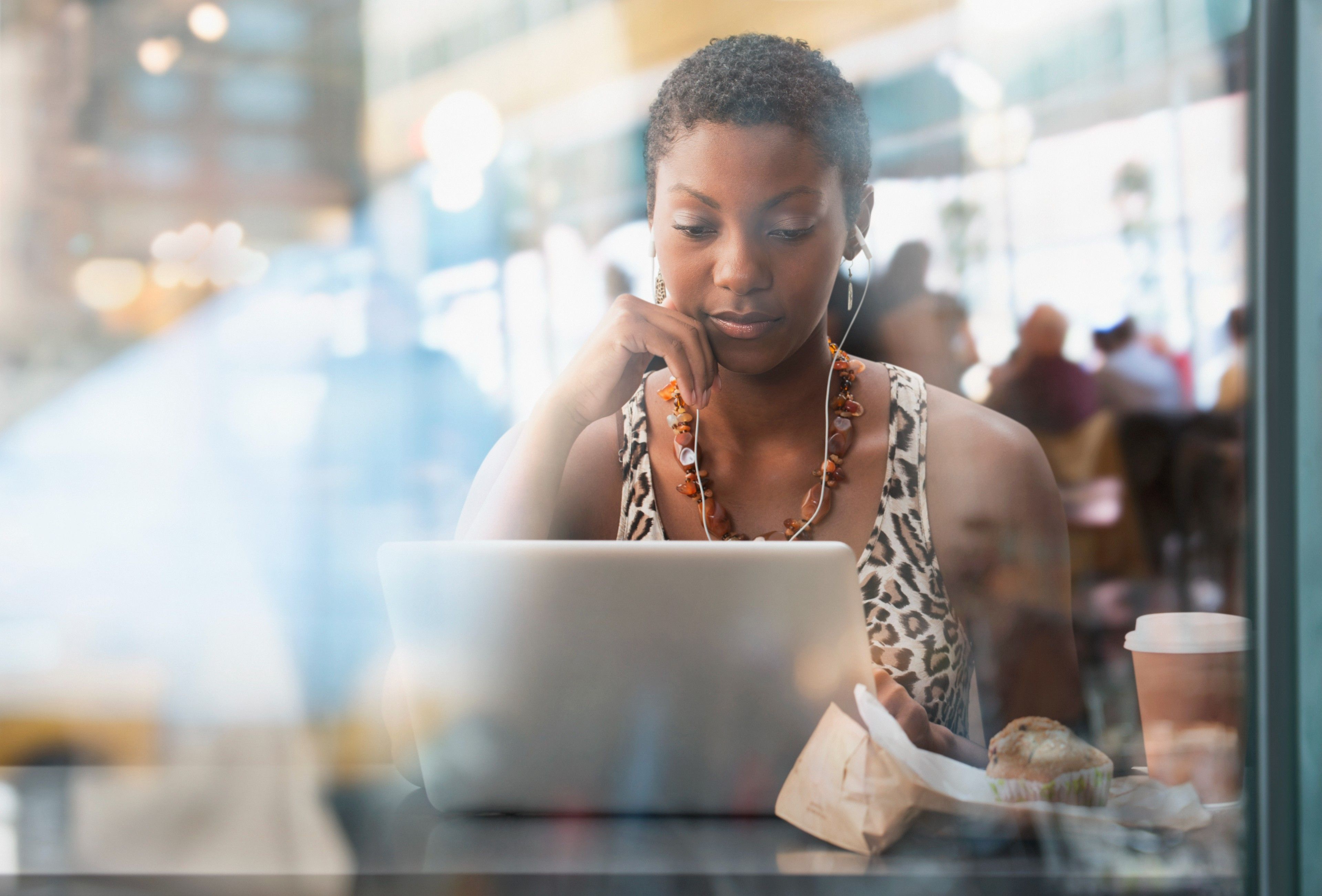 A person working on a laptop in a café with earbuds in, suggesting data access and security.