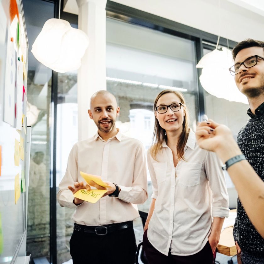 A group of people gather around a whiteboard having a thoughtful discussion.