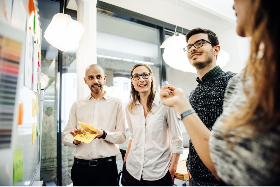 A group of people gather around a whiteboard having a thoughtful discussion.