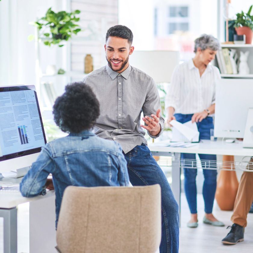 A person sits at a colleagues desk and has an enthusiastic work discussion.